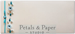 Handcrafted envelope with light blue quilled flowers, pearl accents, gemstones, and a satin ribbon bow on a beige textured background, ideal for invitations and gifting.