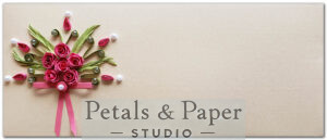 Handcrafted envelope with pink quilled roses, green leaves, pearl accents, gemstones, and a pink ribbon bow on a beige textured background, perfect for weddings and special occasions.