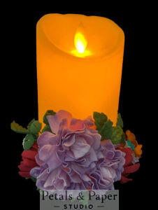 Elegant LED candle with lifelike flickering flame, decorated with handcrafted purple and red flowers and green leaves, perfect for home décor and special occasions.