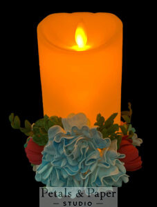 LED flameless candle with realistic flickering flame, surrounded by handcrafted blue and red flowers with green leaves, ideal for home décor, weddings, and celebrations.