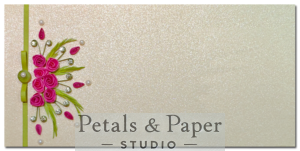Handcrafted 7 x 3.5-inch pearl-finish envelope with deep pink quilled roses, green foliage, a green ribbon with pearl clasp, and pink teardrop embellishments, ideal for weddings and special occasions.