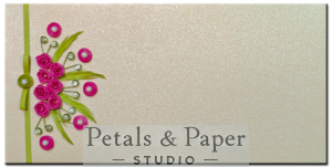 Handcrafted 7 x 3.5-inch pearl-finish envelope with vibrant pink quilled roses, green foliage, rhinestone accents, and a green ribbon clasp, perfect for weddings and special occasions.