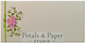 Handmade gift envelope with pink quilled roses, green swirls, rhinestone and pearl accents, and a soft green ribbon on a shimmering textured background, ideal for special occasions.