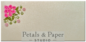 Handcrafted gift envelope with vibrant pink quilled roses, green leaves, pearls, and rhinestones on a shimmering cream background, perfect for weddings and special occasions.