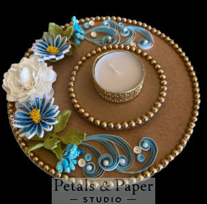 Elegant tea light holder plate with gold beading, blue quilled floral designs, and a gold-rimmed tea light candle centerpiece for home décor and festive celebrations.