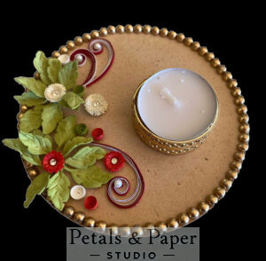 Handcrafted tea light holder plate with red and white floral designs, green leaves, swirling red accents, gold bead edging, and a gold-rimmed tea light for festive and wedding décor.