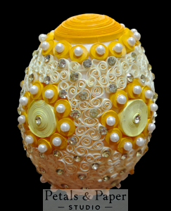 Yellow and white decorative egg with intricate quilling patterns, pearl accents, and rhinestone embellishments, perfect for home decor or seasonal gifting.
