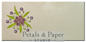 Handmade greeting card with purple quilled roses, green leaves, and pearl accents on a shimmering textured background, perfect for special occasions and heartfelt messages.