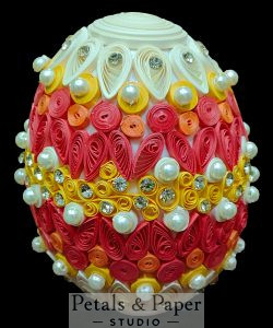 andmade decorative egg with intricate quilling in red, yellow, and cream, adorned with pearls and rhinestones, perfect for elegant home décor.