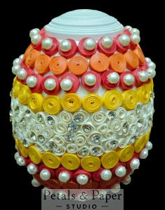 Handmade decorative egg with red, orange, yellow, and white quilling, pearl embellishments, and rhinestone accents, perfect for home décor and gifting.