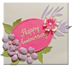 Handmade happy anniversary greeting card with 3D pastel flowers, pearl accents and botanical leaves on pink background