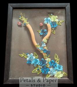 Handcrafted floral letter V shadow box frame with blue and green paper quilling flowers, decorative monogram wall art in black wooden frame for home décor and gifting.